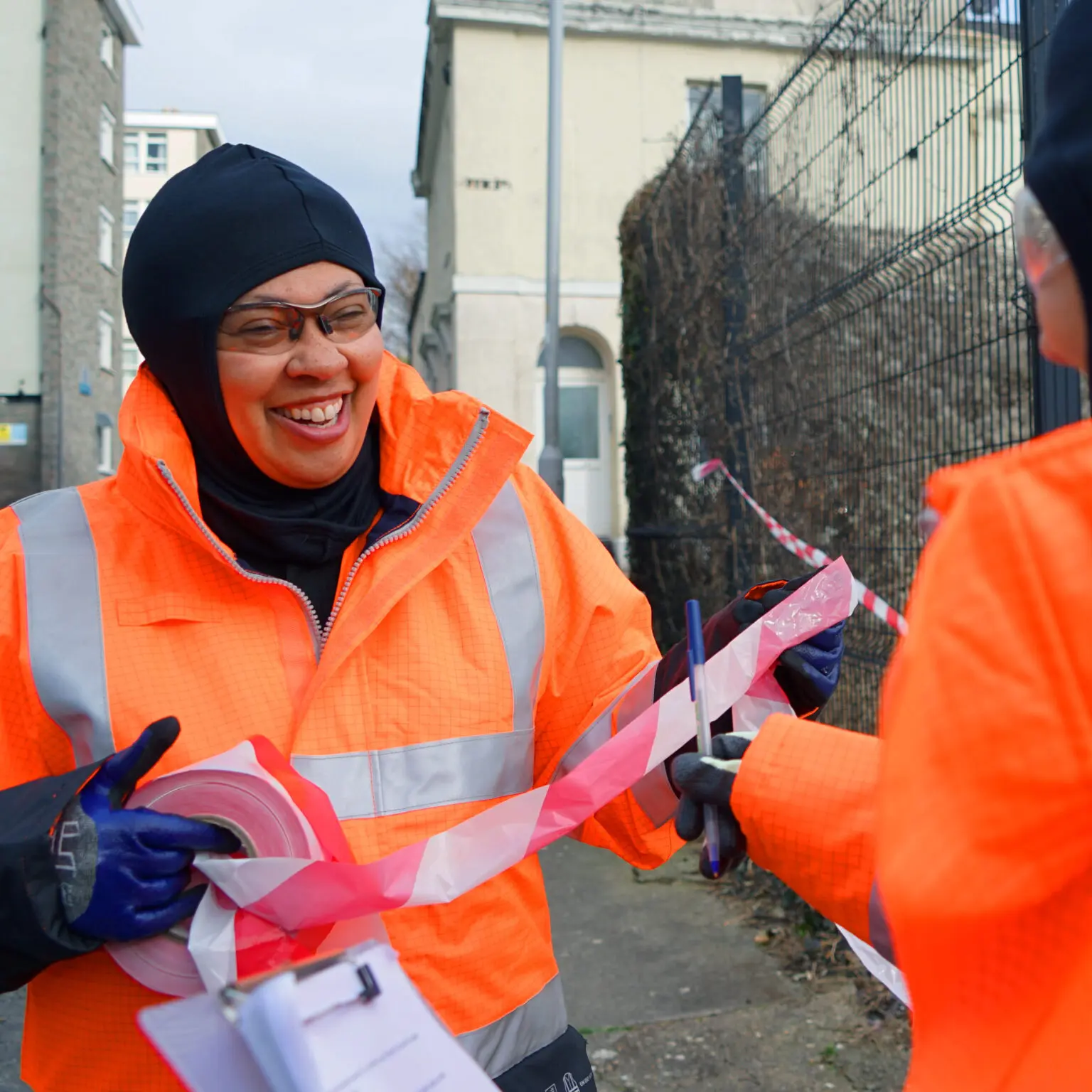 Smiling women in a workwear Hijab, hi-vis jacket, and gloves.