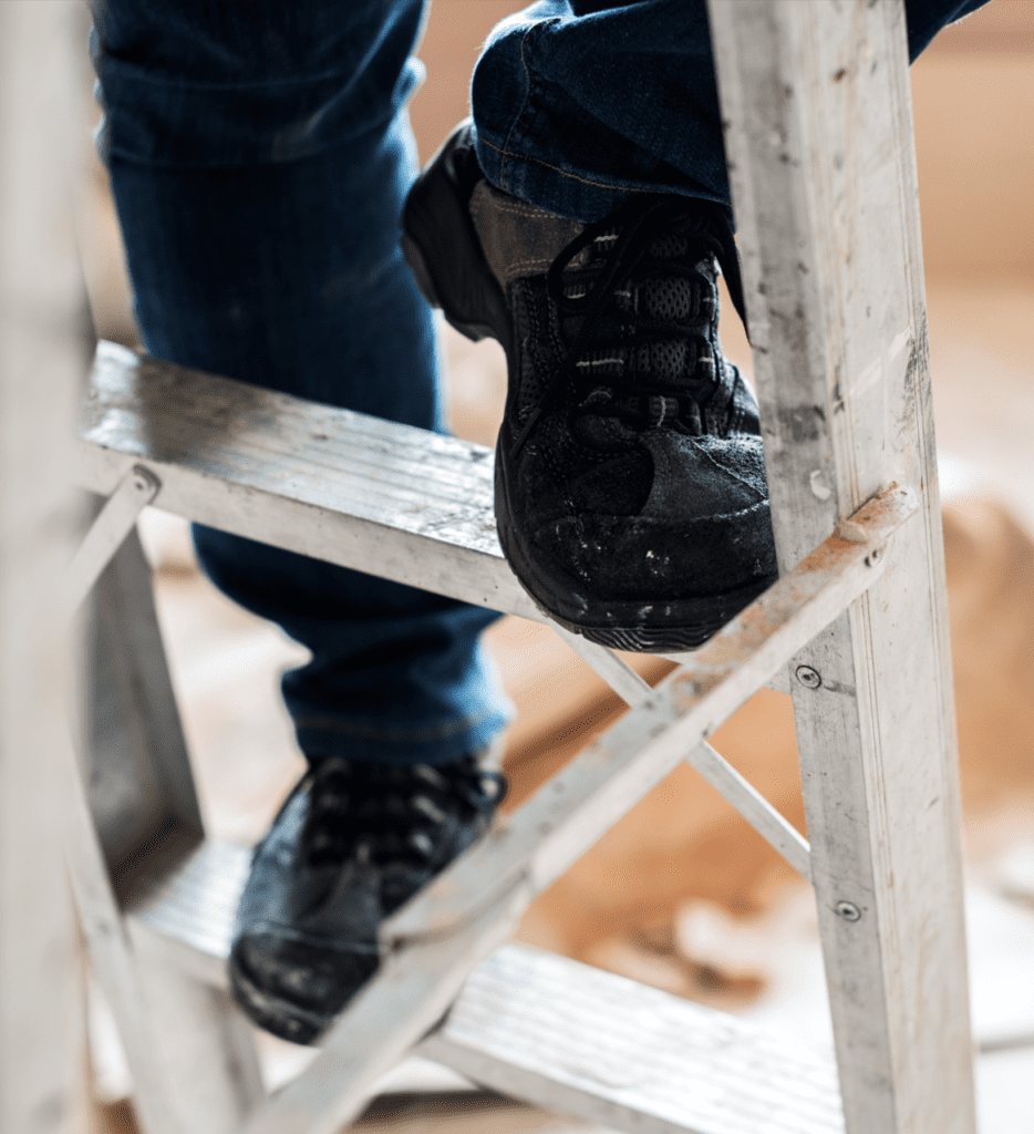 Ladder Safety Decorative Image showing person wearing safety boots climbing ladder, close up.