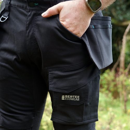 A close up of the Bertee Ecowear EcoStretch trousers being worn with a hand in pocket on a green, woodland background.